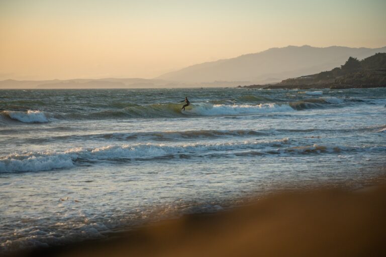 Surfer riding a wave on a beach during a sunset.