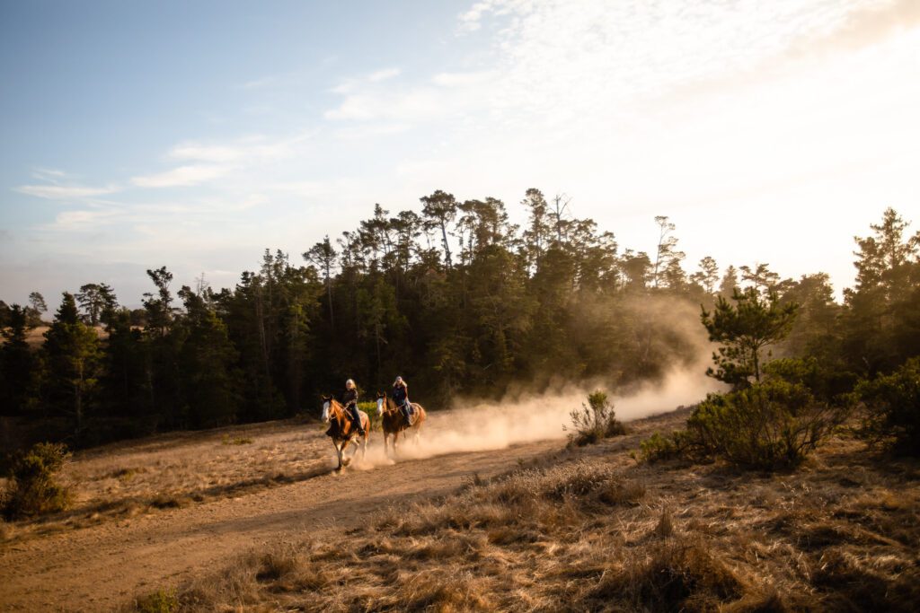 The image depicts people riding horses on a dirt road at Covell Ranch.