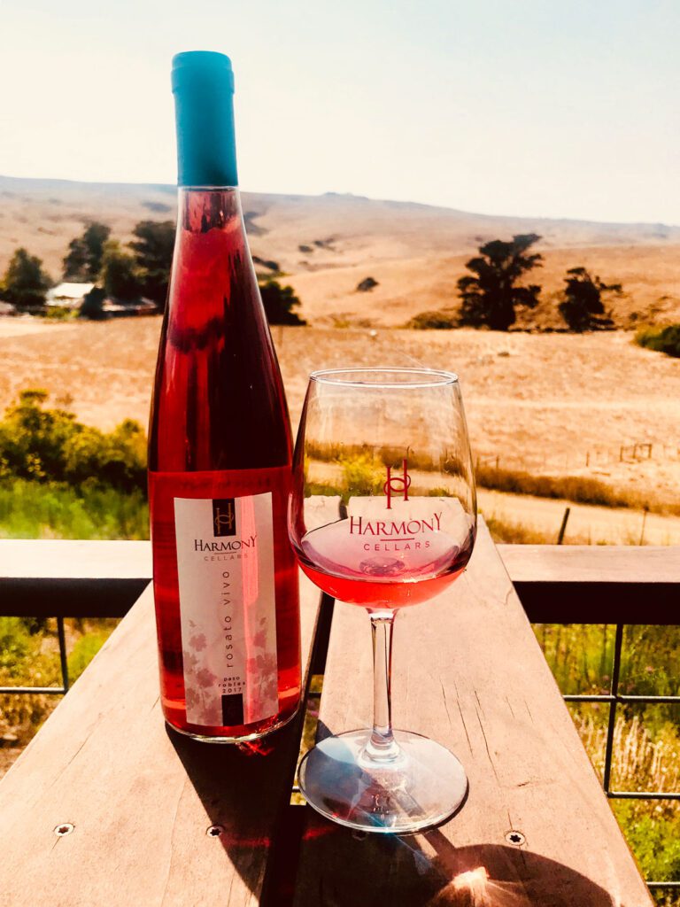 A bottle of red wine and a filled wine glass on a wooden table.