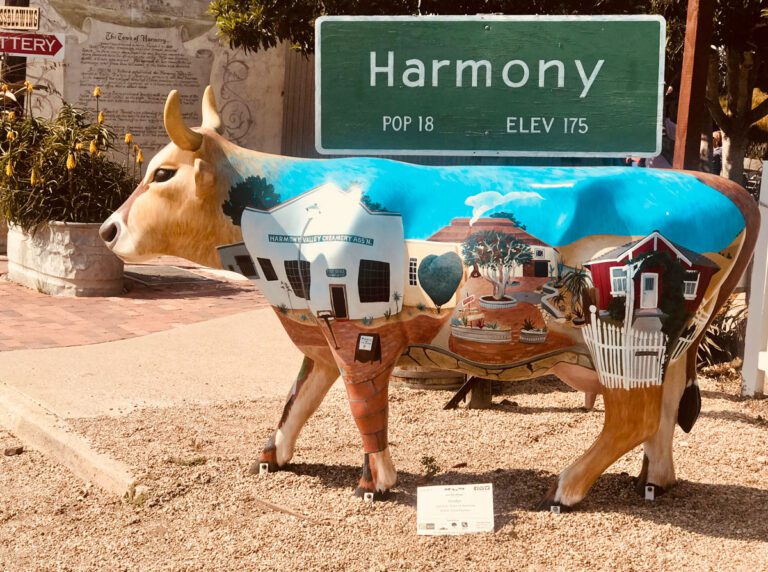 A cow painted like a house stands in front of a sign.