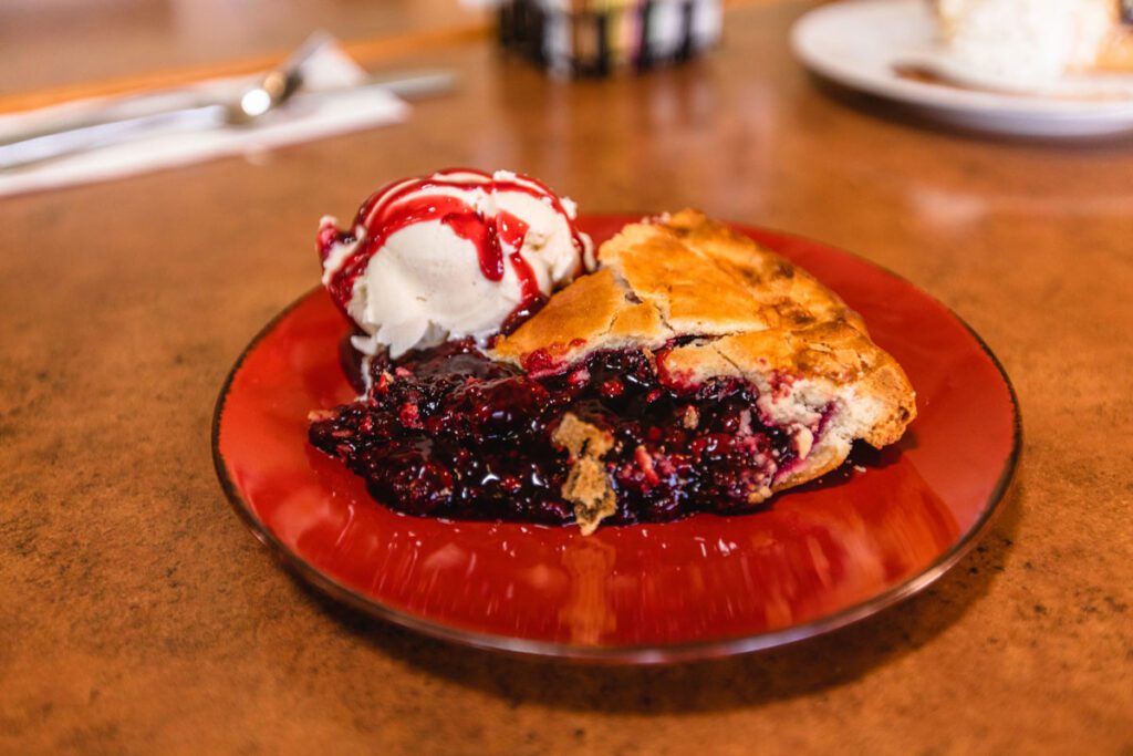 A plate of warm Olallieberry Pie on a plate with whipped cream and strawberry syrup.