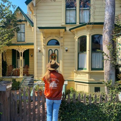 Young-woman-standing-in-front-of-a-victorian-house-in-Cambria-California-Photo-by-Kelsey-Arneson